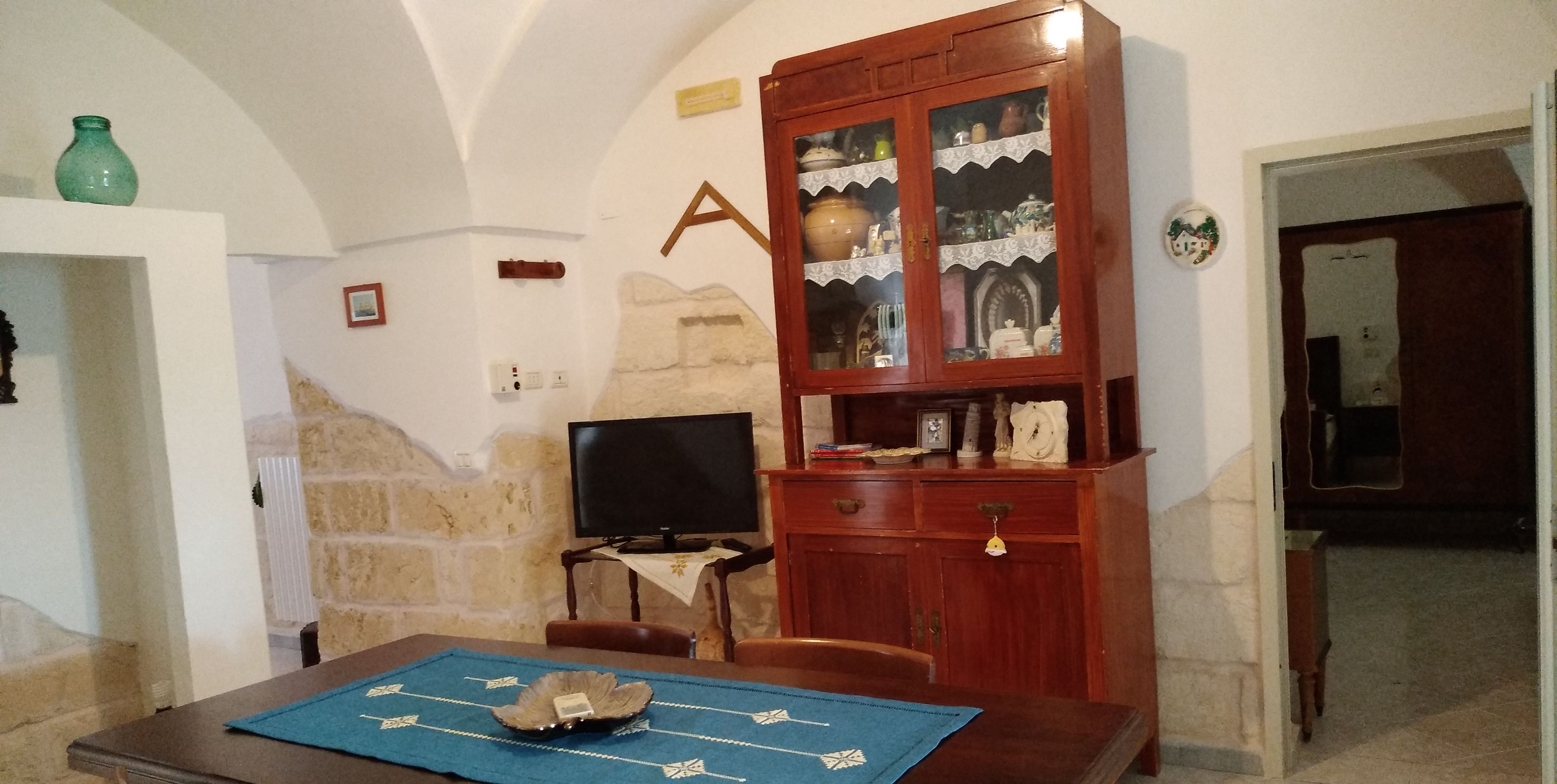 Ein Essbereich mit einer Steinwand, einem Holzschrank mit Glastüren, einem Fernseher und einem Tisch mit einer blauen Tischmatte.