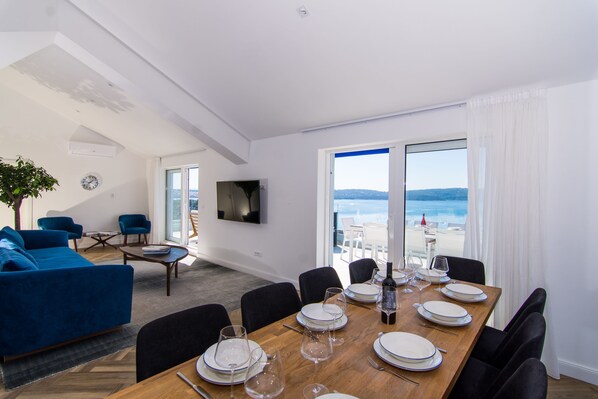 Un comedor con una mesa de madera dispuesta para seis personas, un sofá azul y un televisor fijado a la pared.