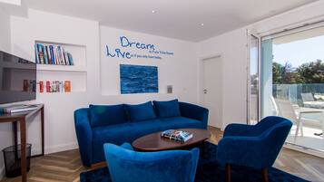 Un salon moderne avec un canapé bleu, un fauteuil assorti et une table basse. On y trouve des étagères remplies de livres et un tableau accroché au mur.
