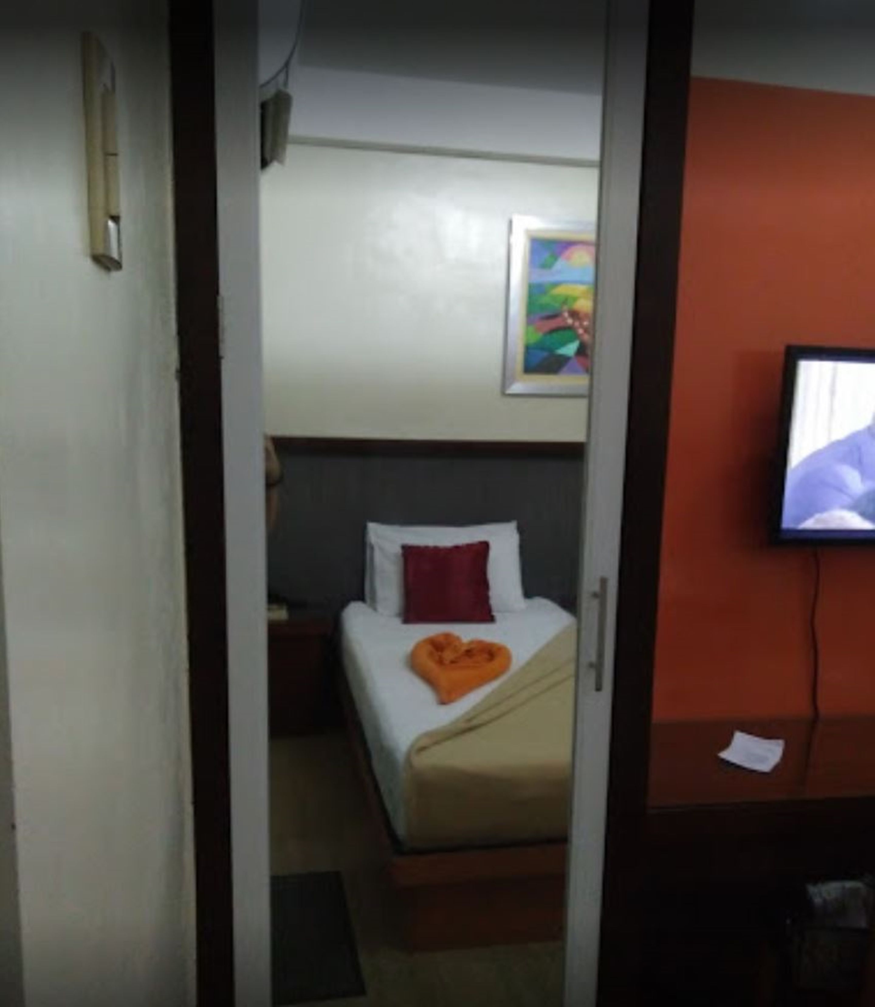 A hotel room with a bed, a nightstand, a television, and a painting on the wall.
