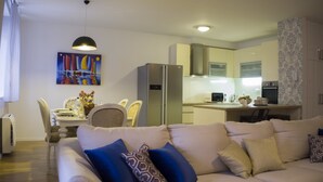 Una sala moderna con sofá, mesa de comedor y sillas. Se ve un refrigerador y un microondas en la cocina.