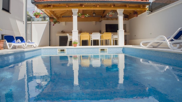 Una piscina con agua azul cristalina, rodeada de sillas de descanso y una pérgola de madera.