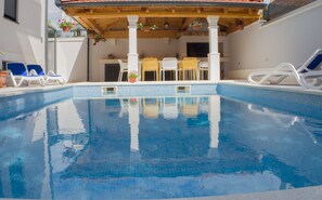 Une piscine à l’eau d’un bleu cristallin, entourée de chaises longues et d’une pergola en bois.