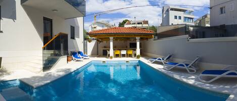 A swimming pool with lounge chairs and a covered seating area.