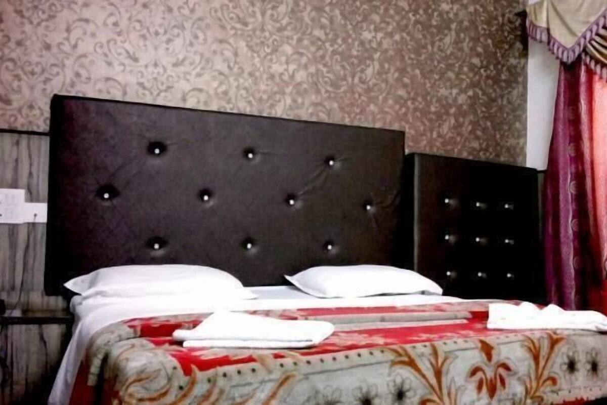 Un lit bien fait, avec une couvre-lit à motifs, une tête de lit capitonnée et un rideau rouge en arrière-plan.