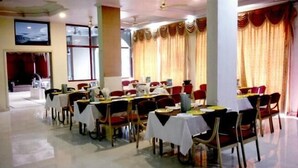 Un espace repas comprenant plusieurs tables et chaises, de grandes fenêtres et des rideaux.