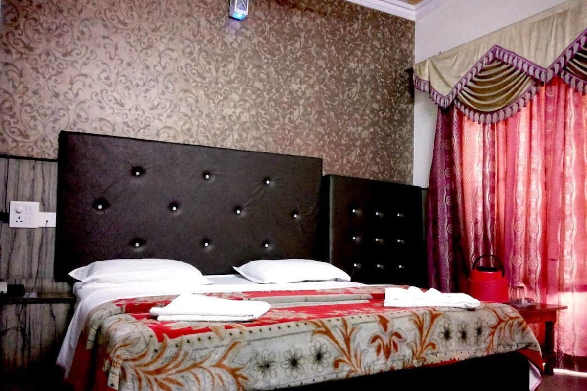 Une chambre à coucher avec un grand lit, une tête de lit sombre, un papier peint à motifs et des rideaux rouges.