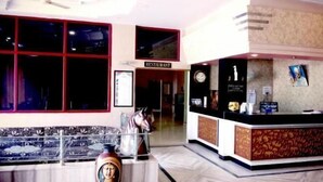 Un hall d’hôtel avec un comptoir d’accueil, une grande fenêtre et un vase décoratif.