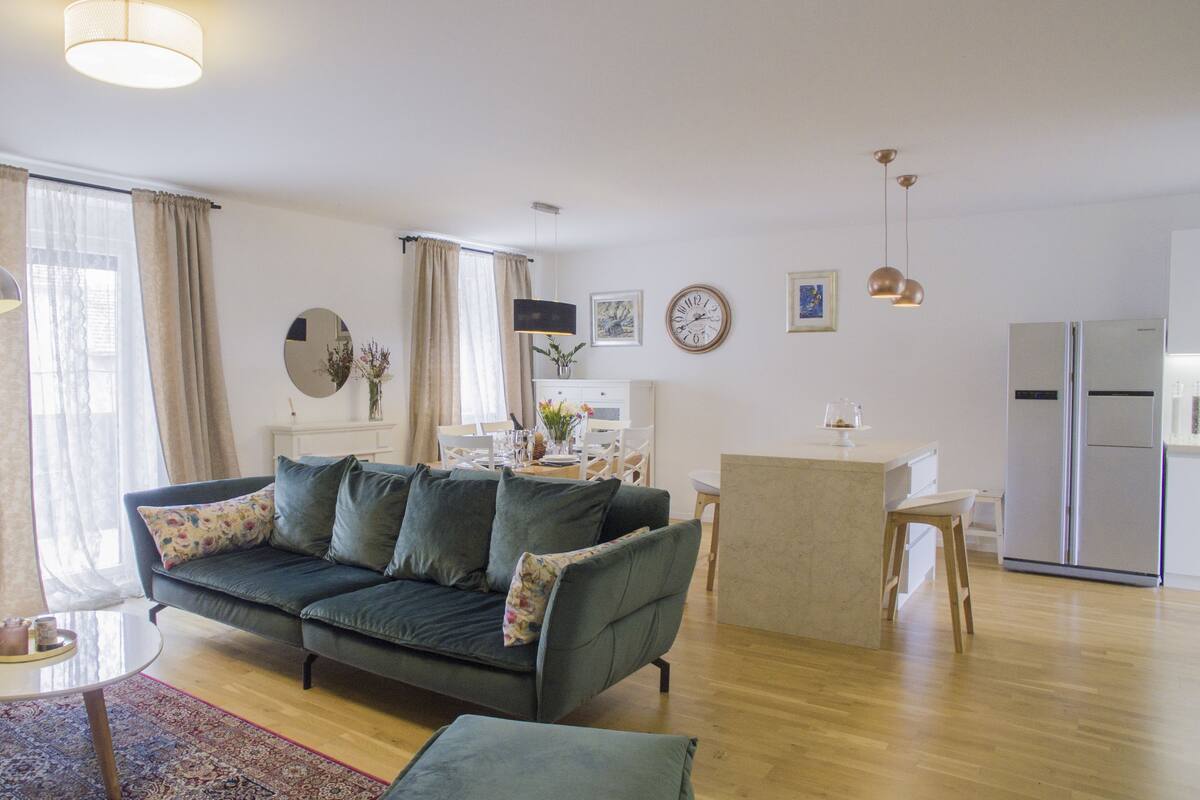 A modern living room with a sofa, a dining table, and a kitchen area.