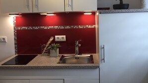 A modern kitchen with white cabinets, a red backsplash, and a granite countertop. - Apartment La Marie (Schwaebisch Gmuend)