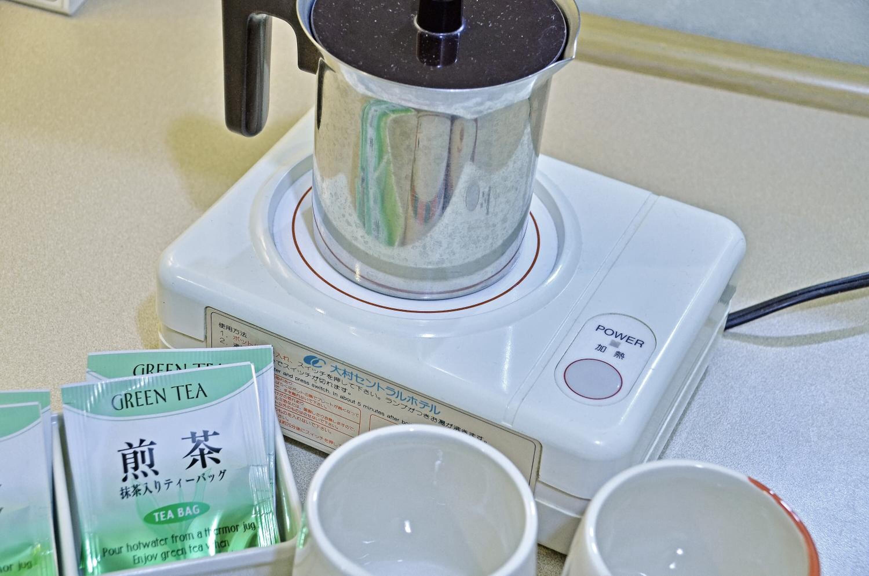 Une machine à café avec une verseuse, un bouton d’alimentation et des sachets de thé, le tout posé sur un plan de travail.