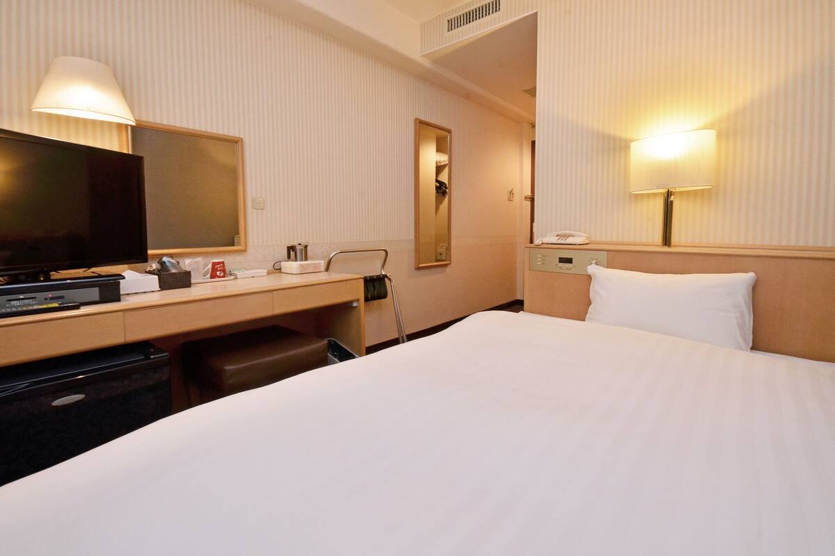 Habitación de hotel con una cama, un escritorio con televisor, un espejo y una lámpara.