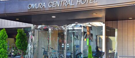 The entrance to Omura Central Hotel with a clear glass facade, bicycles parked outside, and a star-shaped decoration in the foreground.
