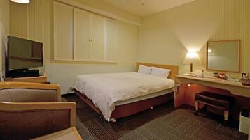 Habitación de hotel con cama, escritorio con lámpara, una silla, televisor y ventana grande.