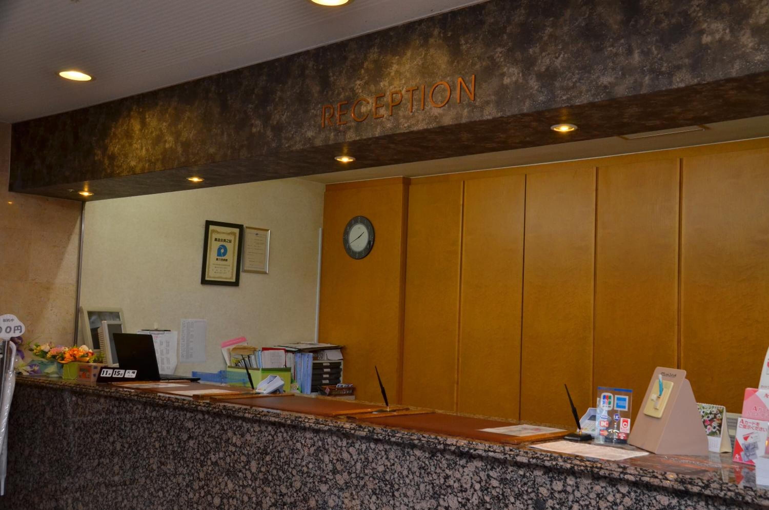 A reception area with a wooden panel wall, a clock, framed certificates, and a reception desk with various items.