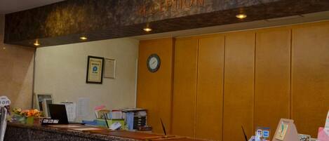 A reception area with a wooden panel wall, a clock, framed certificates, and a reception desk with various items.