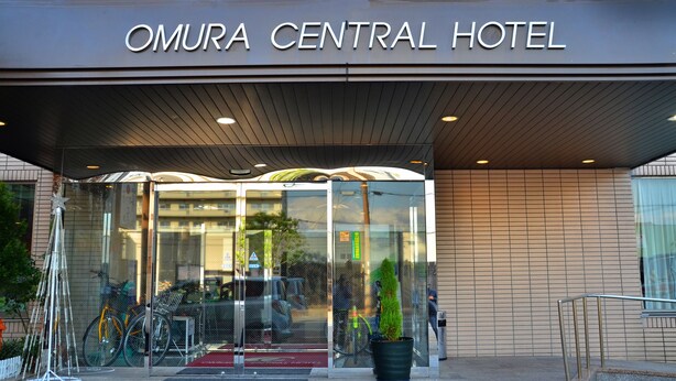 Der Eingang des Omura Central Hotels mit Glasfassade, rotem Teppich und abgestellten Fahrrädern.