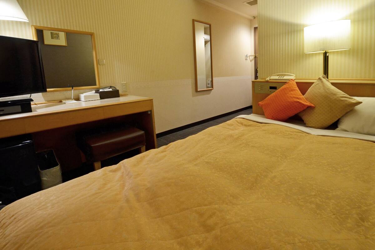 Una habitación de hotel con una cama, un escritorio con televisor, un espejo y una lámpara.