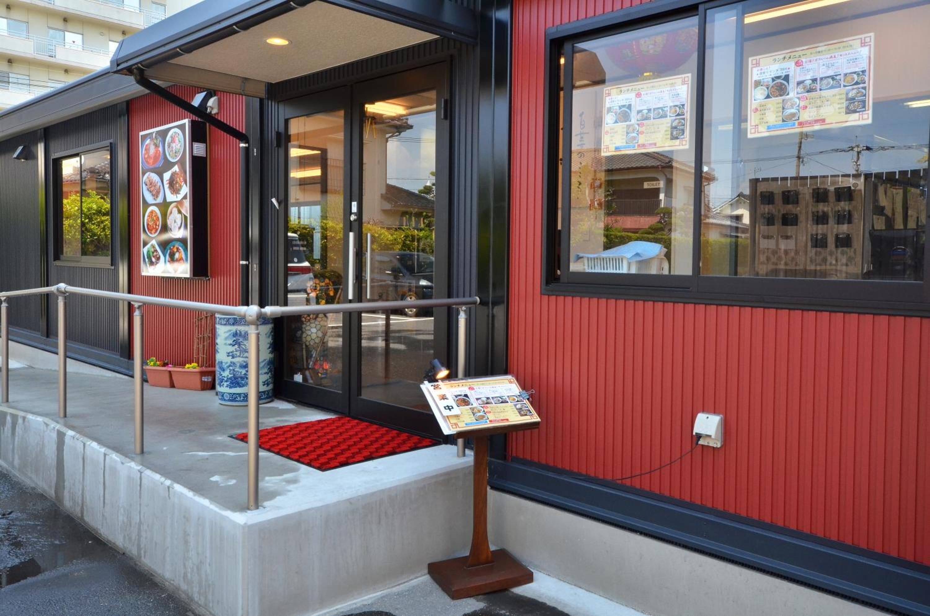 Un restaurante con fachada roja, puerta de cristal y un expositor de menú en el exterior.