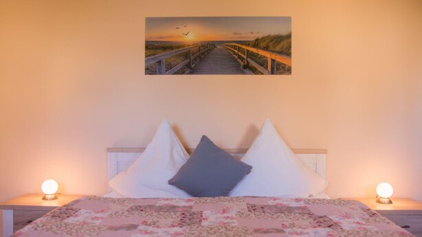 Un dormitorio con una cama, dos lámparas de noche, una colcha de flores y un cuadro de atardecer en la pared.