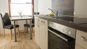 Cocina compacta con horno empotrado, estufa y ventana con persianas.