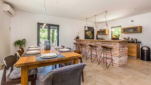 A modern kitchen with a brick island, bar stools, and a dining area with a wooden table and chairs. - Holiday house RASOPASNO (Rasopasno)