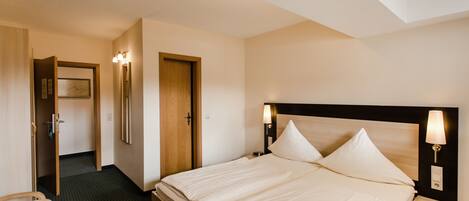 Una habitación de hotel con una cama, mesitas de noche, un escritorio y una puerta.