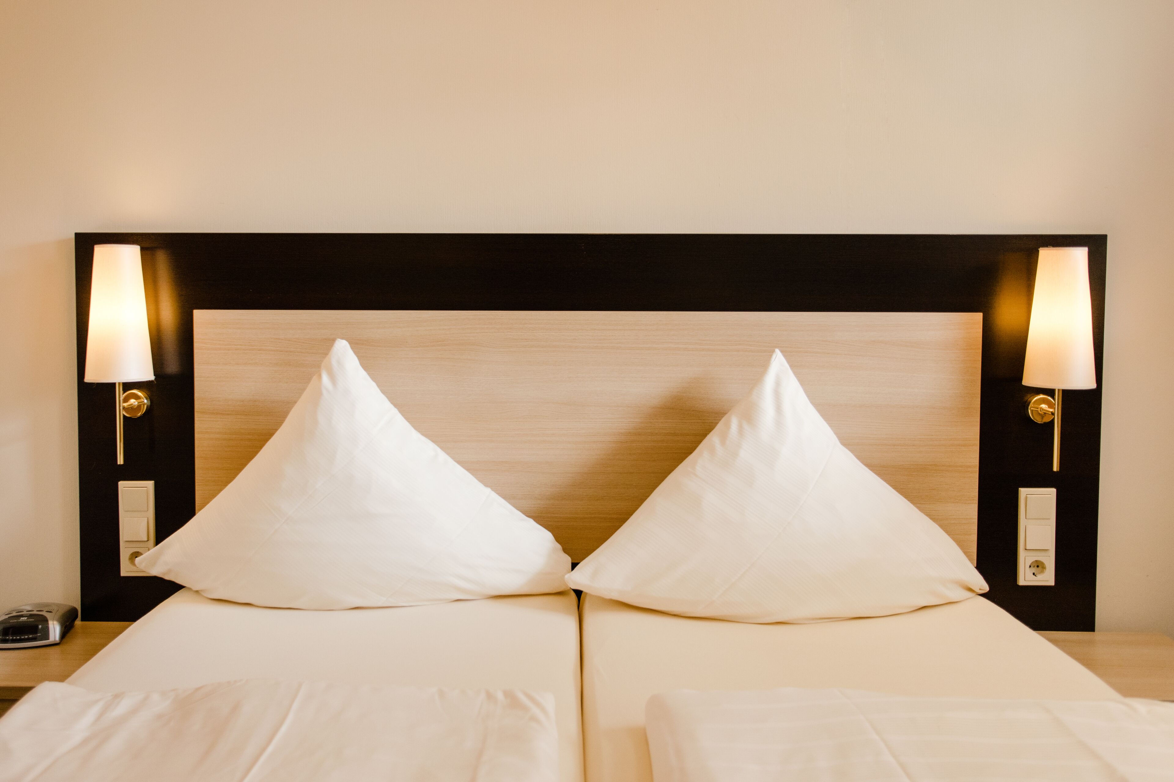 Una cama doble con cabecera de madera, dos lámparas de noche y una mesita de noche con un teléfono.
