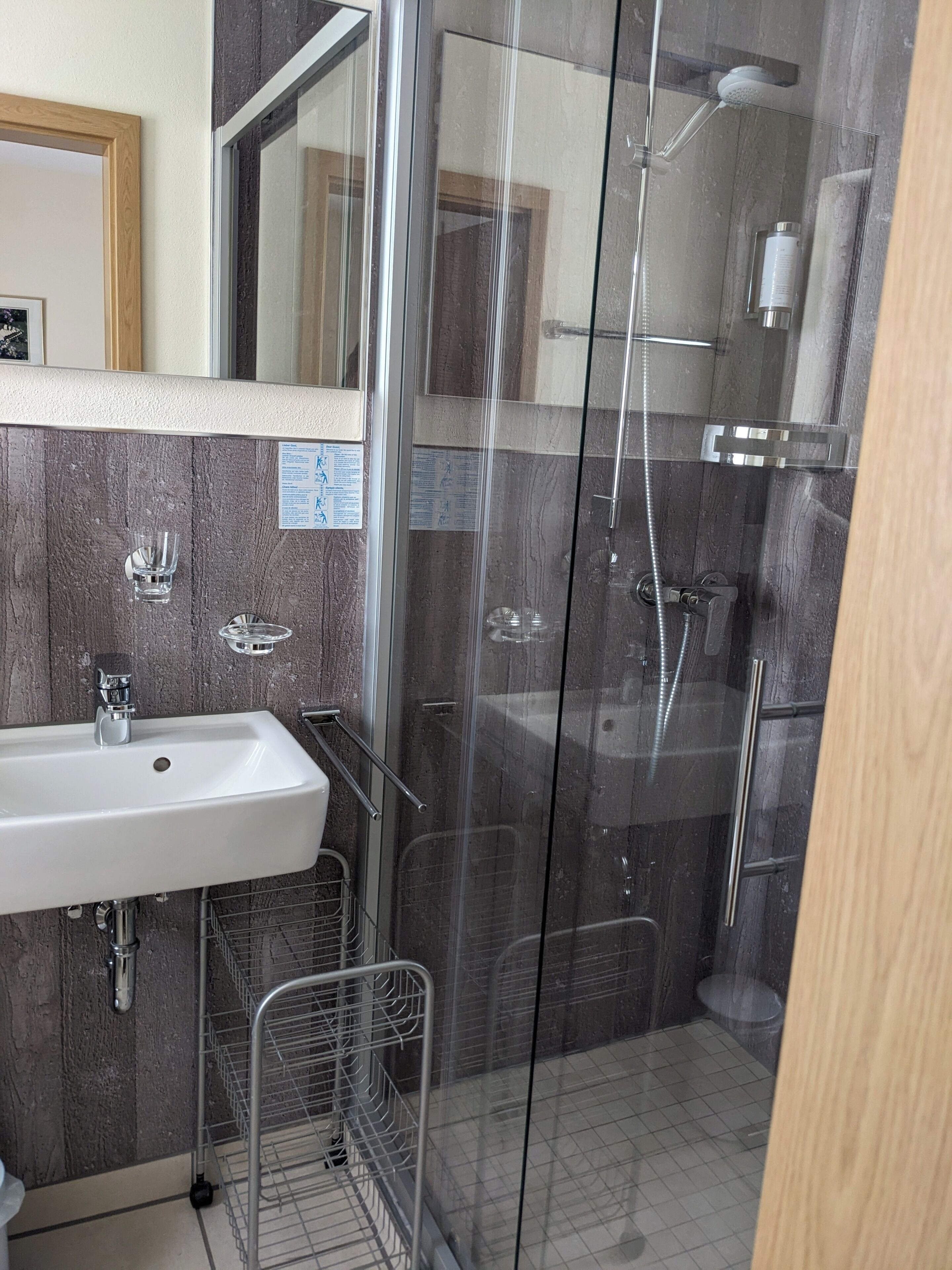 Een badkamer met een glazen douchecabine, een wastafel met een metalen rek en een spiegel boven de wastafel.
