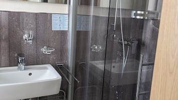 Ein Badezimmer mit einer Duschkabine, einem Waschbecken mit einem Metallregal und einem Spiegel darüber.