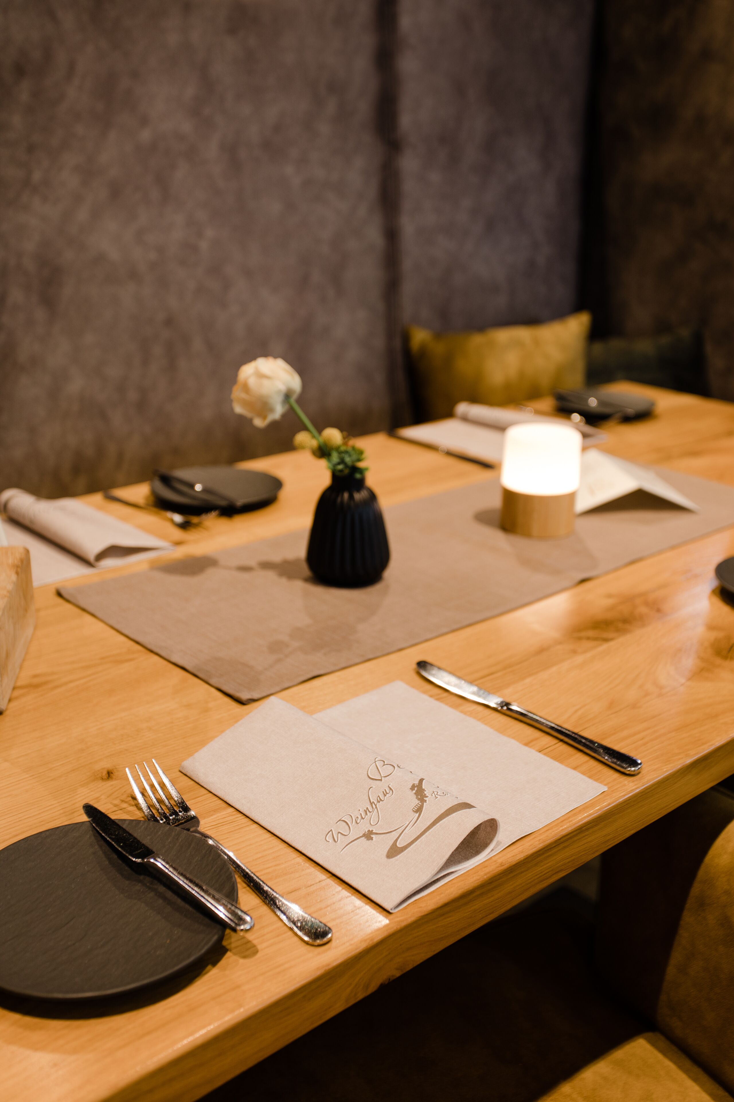 A dining table set with a candle, a vase with a single flower, and a menu.