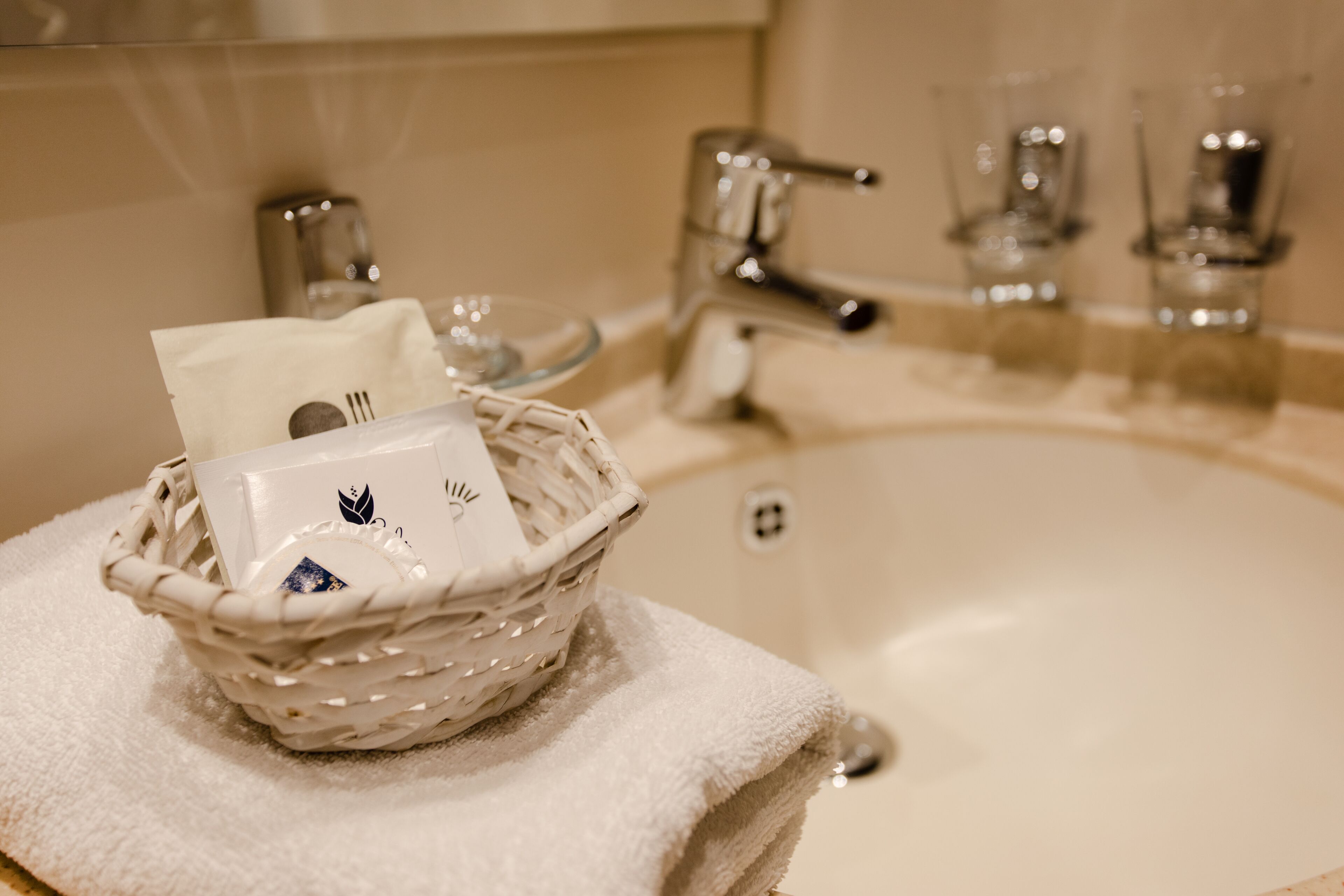 A bathroom sink with a white towel, a basket containing toiletries, and a glass of water.