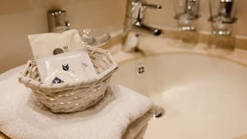 Un lavamanos de baño con una toalla blanca, una cesta con artículos de aseo y un vaso de agua.