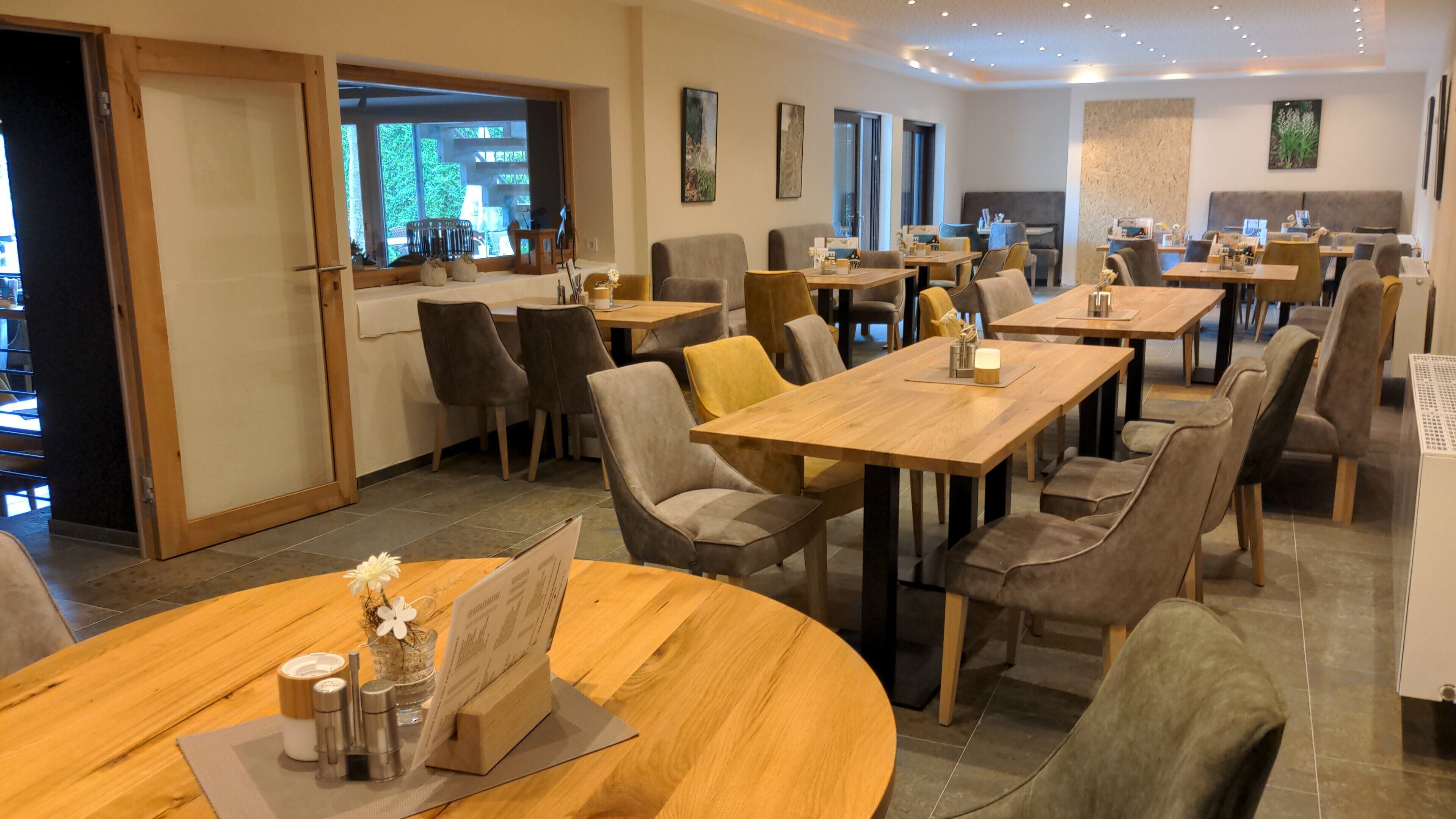 Un restaurant doté de nombreuses tables et chaises, d’un plancher en bois et offrant une vue sur l’extérieur grâce à une grande fenêtre.
