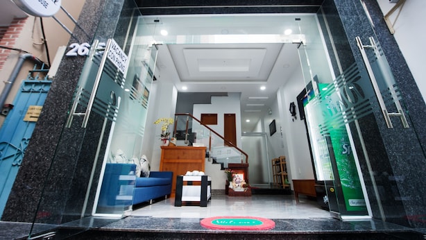 A hotel entrance with a reception desk, a staircase, and a blue sofa. - The White House (Ho Chi Minh City)
