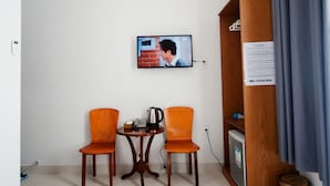A room with two orange chairs, a small wooden table with a kettle and a phone, a television mounted on the wall, and a wooden cabinet with a passcode sign. - The White House (Ho Chi Minh City)