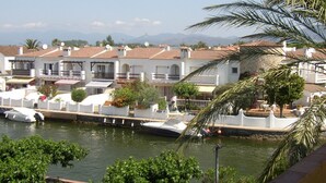 Un quartier résidentiel en bord de mer, avec des bâtiments blancs, une marina et une vue dégagée sur la mer et les montagnes en arrière-plan.