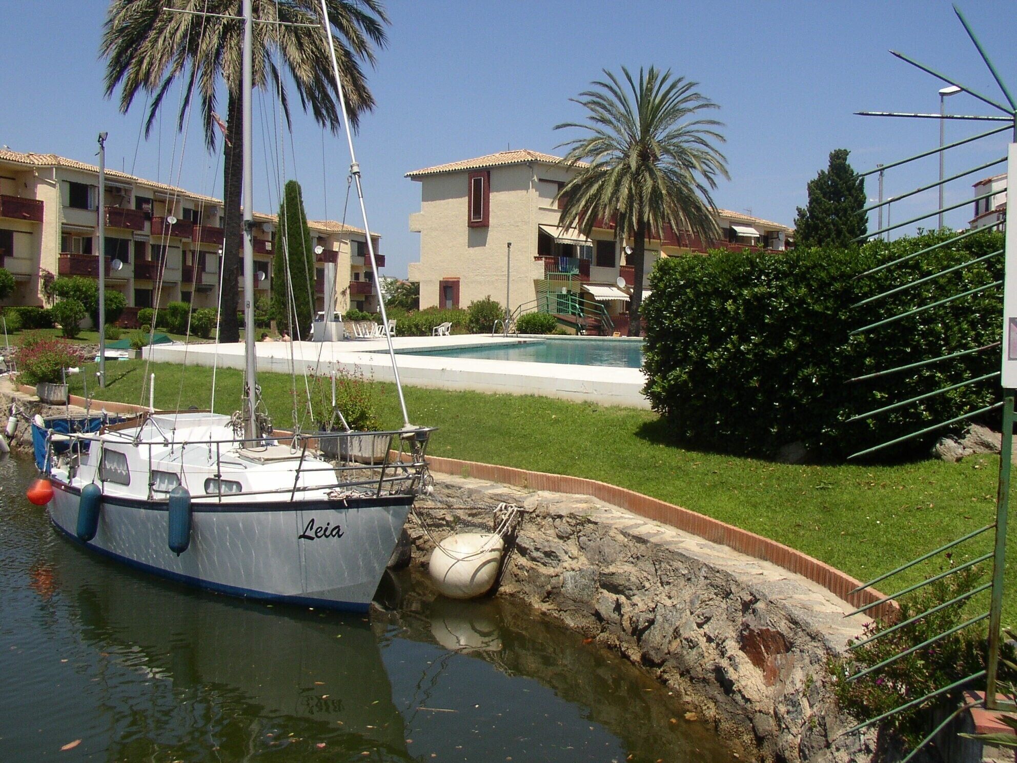Un port de plaisance où est amarré un bateau appelé « Leia », une piscine et, au fond, des immeubles d’habitation.