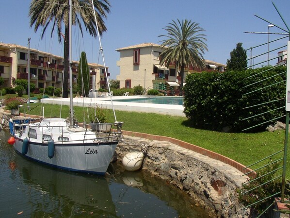 Un puerto deportivo con un barco llamado "Leia" amarrado, una piscina y edificios residenciales al fondo.