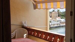 Un balcon doté d’un auvent à rayures, d’une chaise blanche et offrant une vue sur une étendue d’eau et des bâtiments.