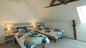 Ein Schlafzimmer mit zwei Betten, Holzbalken, einem Oberlicht und einem Nachttisch mit Lampe.