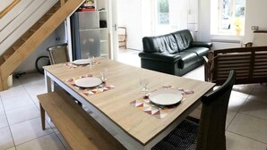 Ein Essbereich mit einem Holztisch, gedeckt für zwei Personen, einer schwarzen Ledersofa und einer Treppe.
