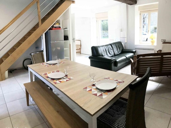 Un coin repas avec une table en bois dressée pour deux personnes, un canapé en cuir noir et un escalier.