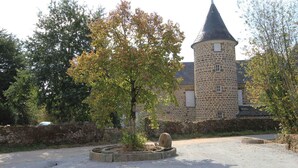Ein Steinhaus mit einem Turm, umgeben von Bäumen und einem Kiesweg.