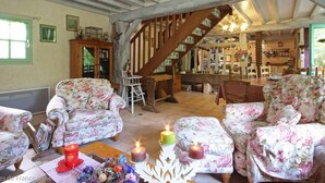 Un salon chaleureux, avec des meubles à motifs floraux, un escalier et un coin cuisine visible au fond.