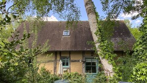 Une maison traditionnelle avec un toit en tuiles, entourée d’une végétation luxuriante et dotée d’une terrasse dallée.