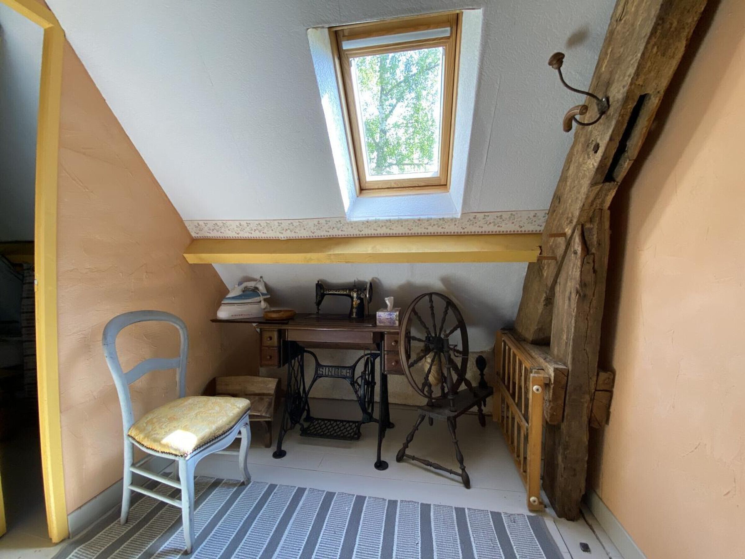 Une petite pièce agréable, dotée d’un plafond en pente, d’une machine à coudre, d’une chaise et d’une fenêtre.