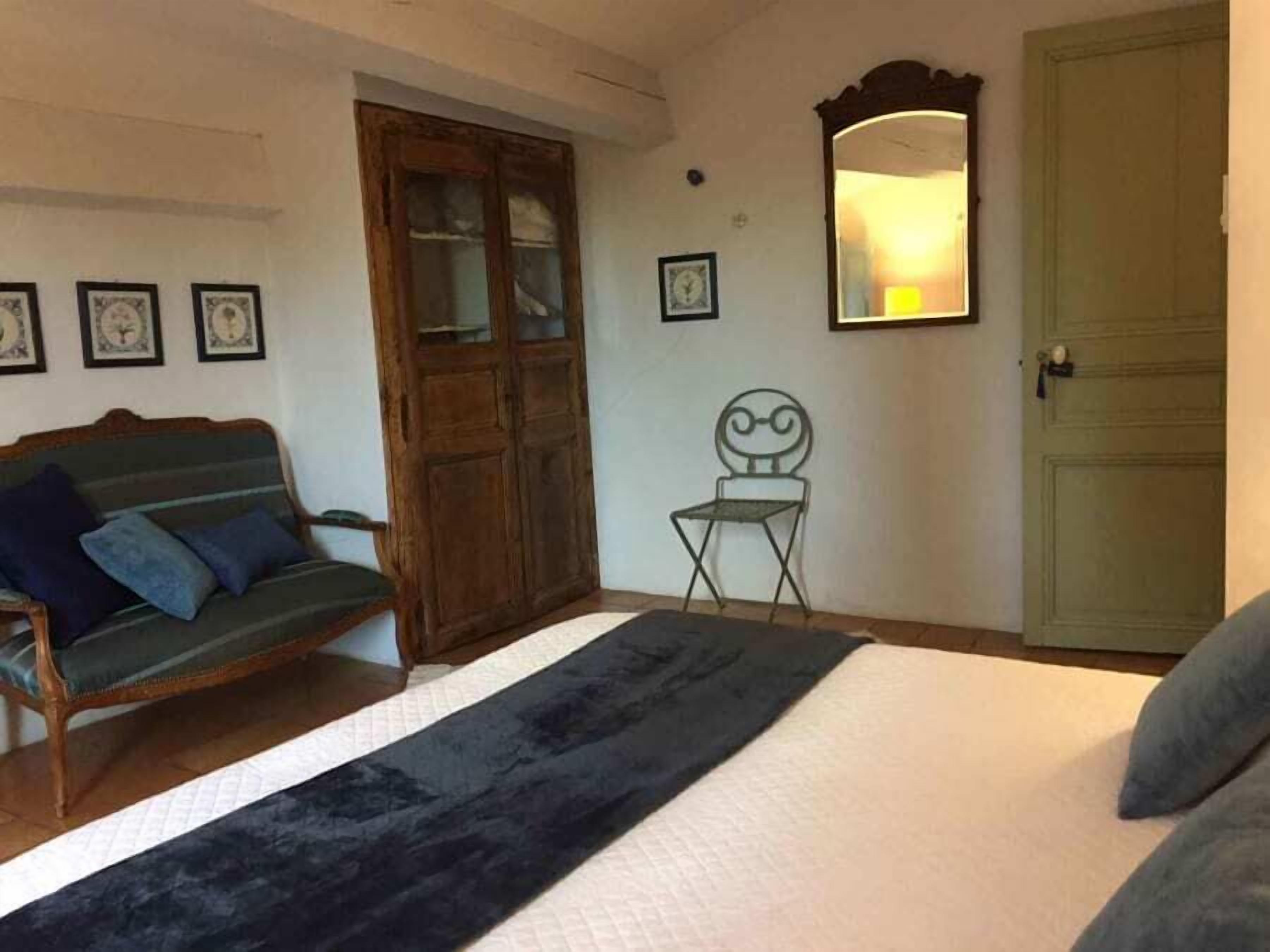 A bedroom with a bed, a wooden wardrobe, a small chair, and a mirror on the wall.