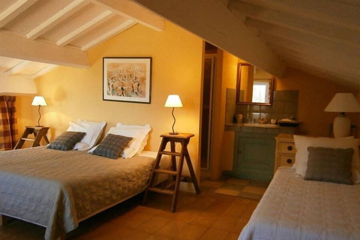Camera accogliente con due letti, una scala in legno, uno sgabello e un angolo cottura con lavello e pensili.