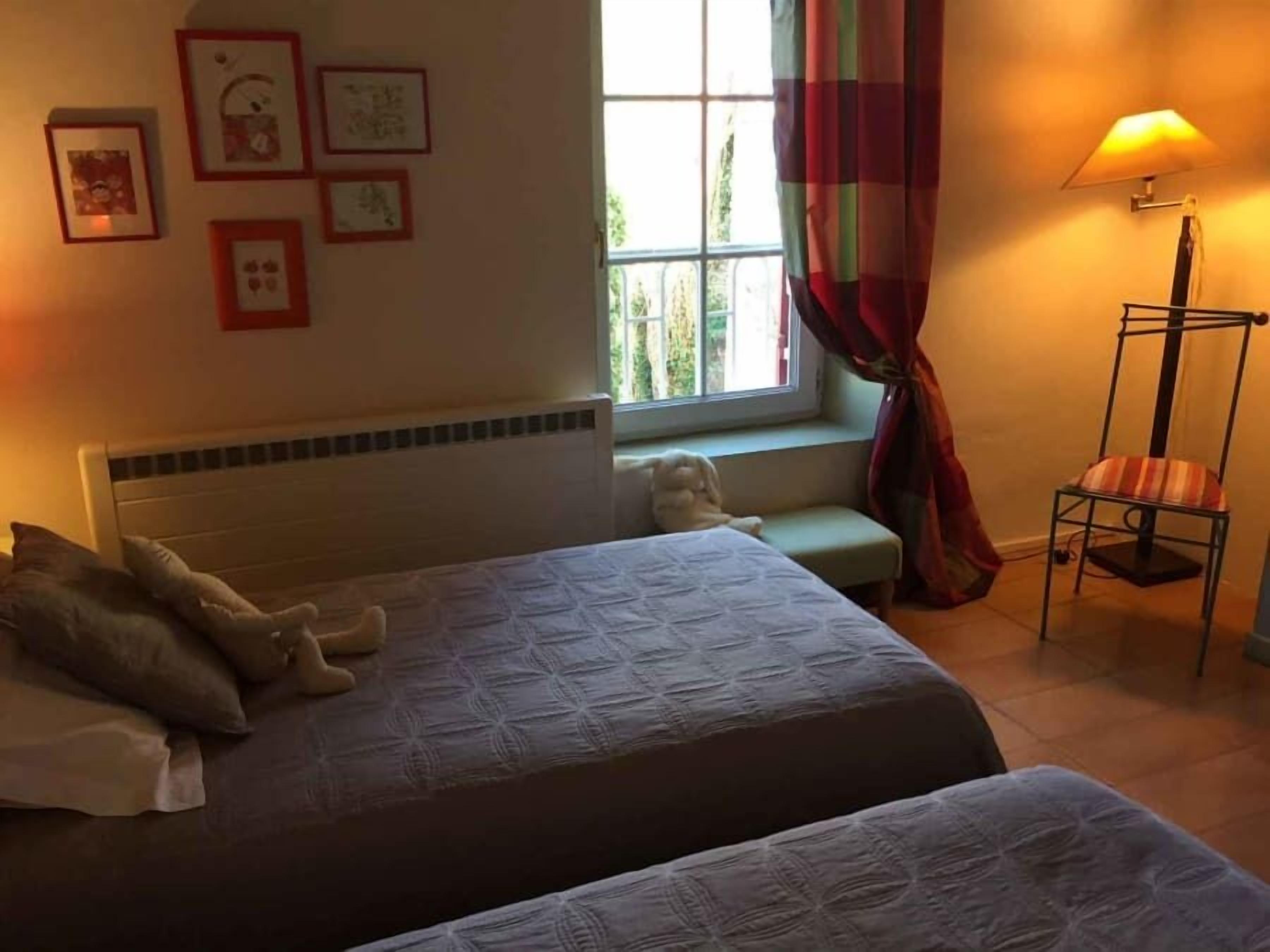 A hotel room with two beds, a window with curtains, a floor lamp, and framed pictures on the wall.